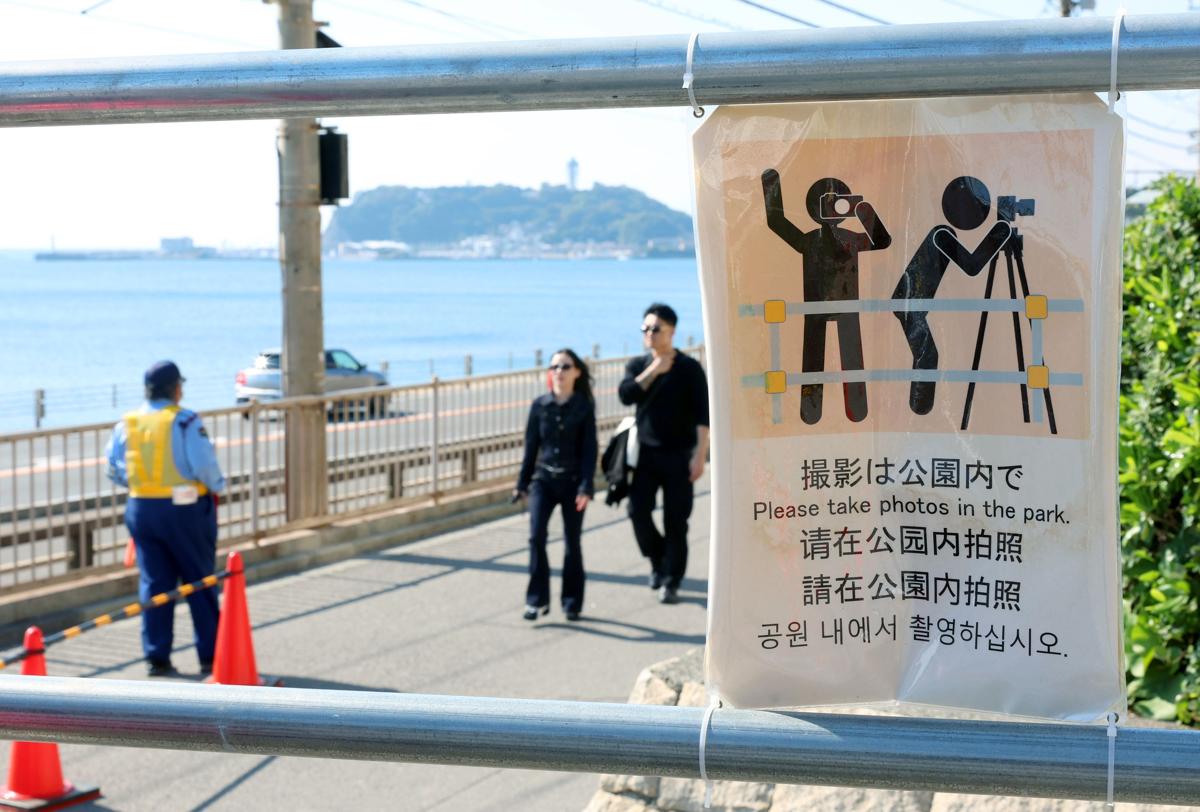 
注意を呼びかけるチラシも多言語だ。奥に見えるのは江ノ島。国内の観光客で、踏切周辺に立ち寄る人も多い＝10月、鎌倉市
