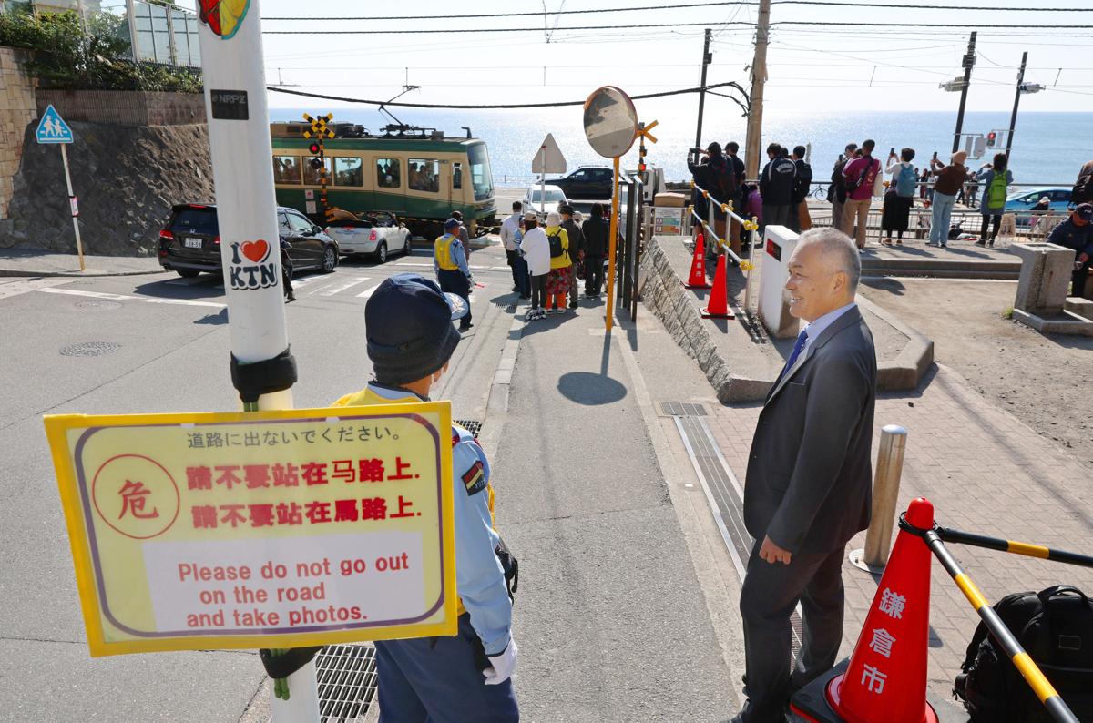 
警備員と話す「鎌倉ガーディアンズ」代表の大津定博（右）。「スラムダンクの踏切」には多くの観光客が訪れている＝１０月、神奈川県鎌倉市
