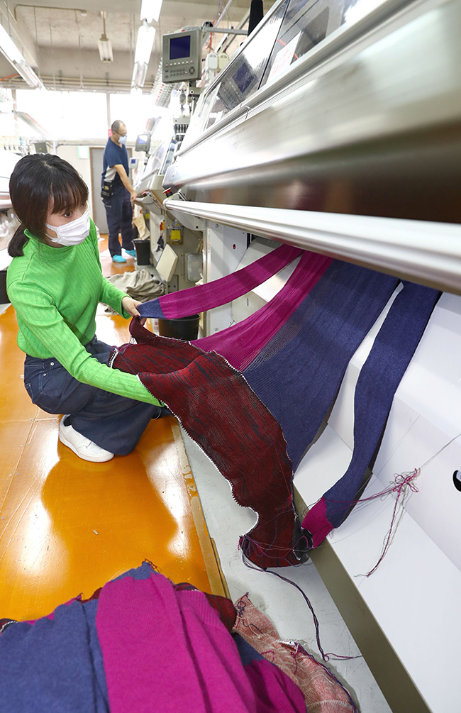 完成した形でウエアを編み上げる無縫製編み機。ワンピース、カーディガンなどが１、２時間で姿を現す＝見附市新町２の丸正ニットファクトリー