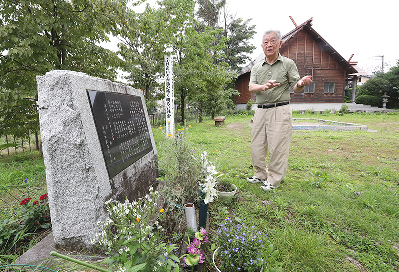 空襲後の神明神社の様子を父から聞いた今泉弥さん。手前は犠牲者を悼む慰霊碑＝長岡市柳原町