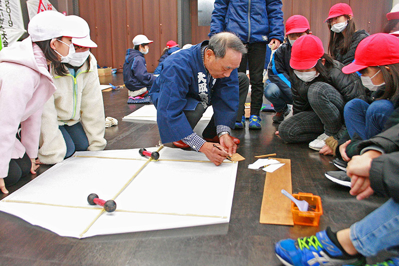 今町小の児童に大凧の作り方などを教える大凧合戦協会の職人＝１月、見附市今町１