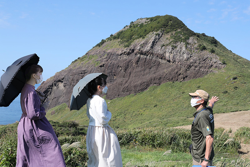 雄大な姿を見せる大野亀。初夏にはトビシマカンゾウの黄色い花が一面を鮮やかに彩る＝佐渡市願