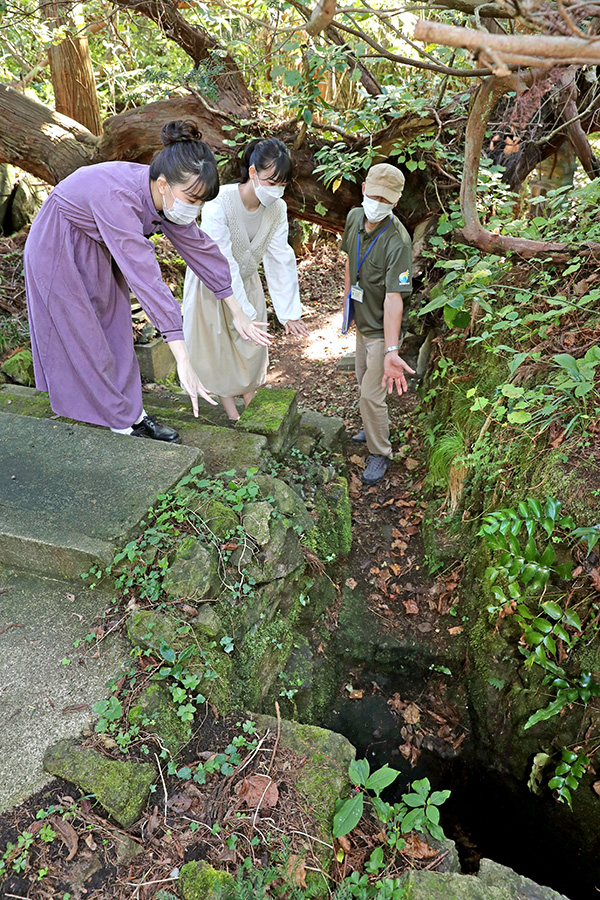寒戸狸が住んでいたと伝わる風穴。冷たい風を感じる。右はジオパークガイドの池善世さん＝佐渡市関
