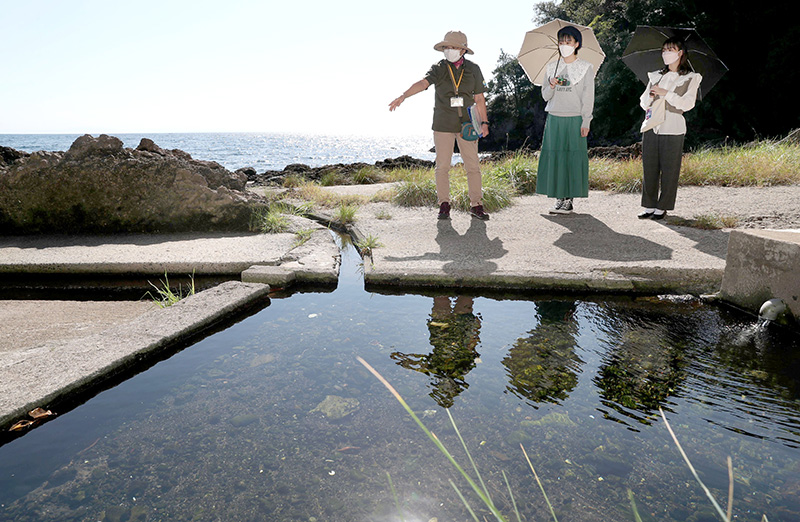 「弘法水」と呼ばれる湧き水の前で祝雅子さん（左）の説明を聞く横山実郁さん（中）と宇野友恵さん＝佐渡市元小木地区