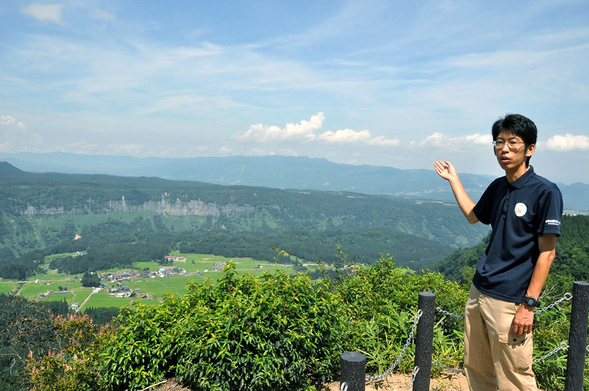 「谷の展望台」を案内する佐藤信之さん。縄文時代から地形の大きな変化はなく「縄文人が見ていた景色と一緒なんですよ」と語る＝津南町
