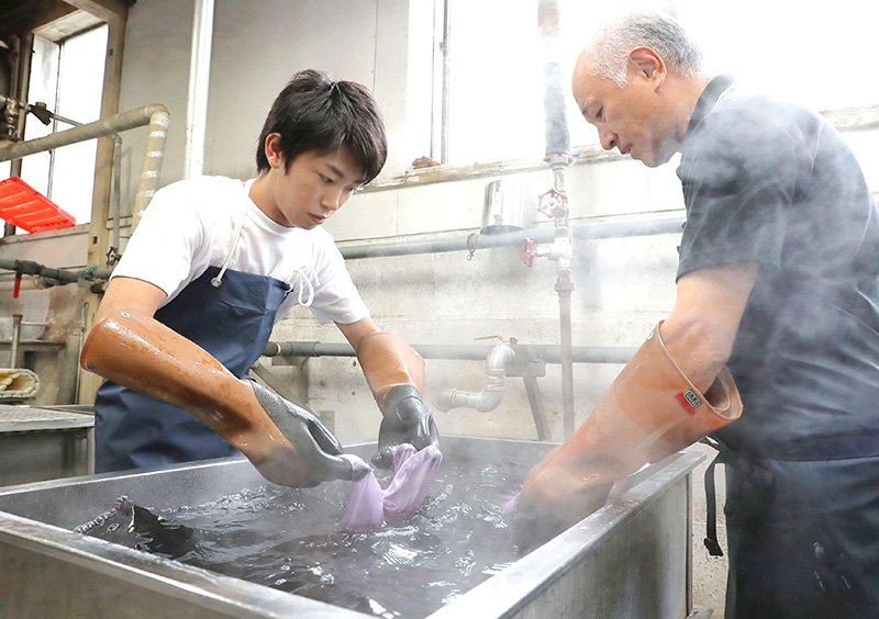 液温約９０度の染料の中に、絞り染めのハンカチを浸す加藤さん＝十日町市明石町