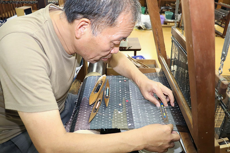 伝統的工芸品「十日町絣」を伝承する渡吉織物の渡辺孝一さん。近年は、図案に合わせて色糸を織り込む「すくい」の技術も併用し、表現の幅を広げている